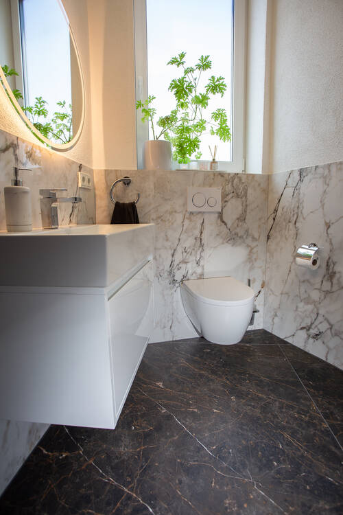 Fertig gefliestes Bad: Wandverkleidung in heller Marmoroptik mit sauberem Fugenbild, dunkler Marmorboden, Waschtisch und Wand-WC