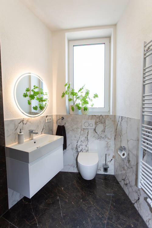 Von FliesWerk gefliestes Bad: halbhohe Wandverkleidung in weißer Marmoroptik, dunkler Marmorboden, Waschtisch und Wand-WC