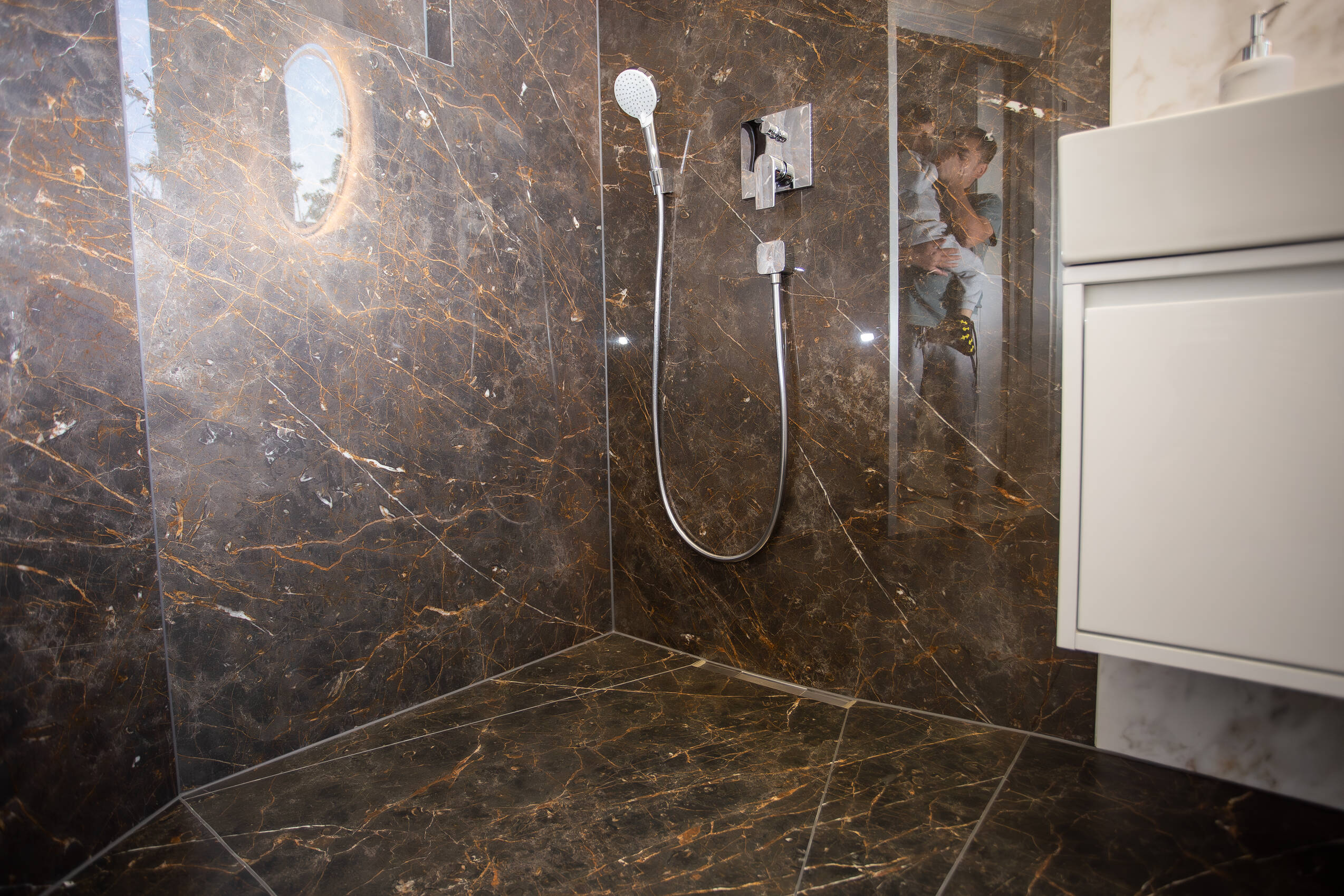 Von FliesWerk saniertes Bad: bodengleiche Dusche mit großformatigen Wandplatten in dunkler Marmoroptik, Unterputz-Armatur und Gefälle zur Duschrinne